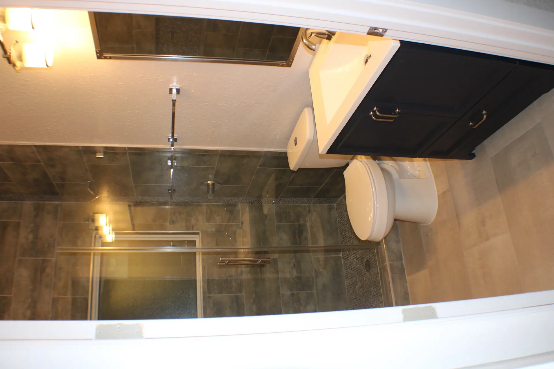 Master bathroom with dual vanities featuring dark wood cabinetry, white countertops, and large-format gray stone tile walls in the 111 Marina coastal cottage