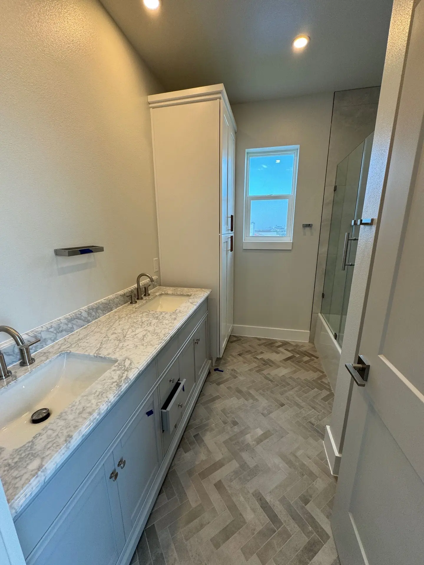 Primary bathroom with gray vanity, white marble countertop, brass faucet fixtures, and frameless glass shower enclosure