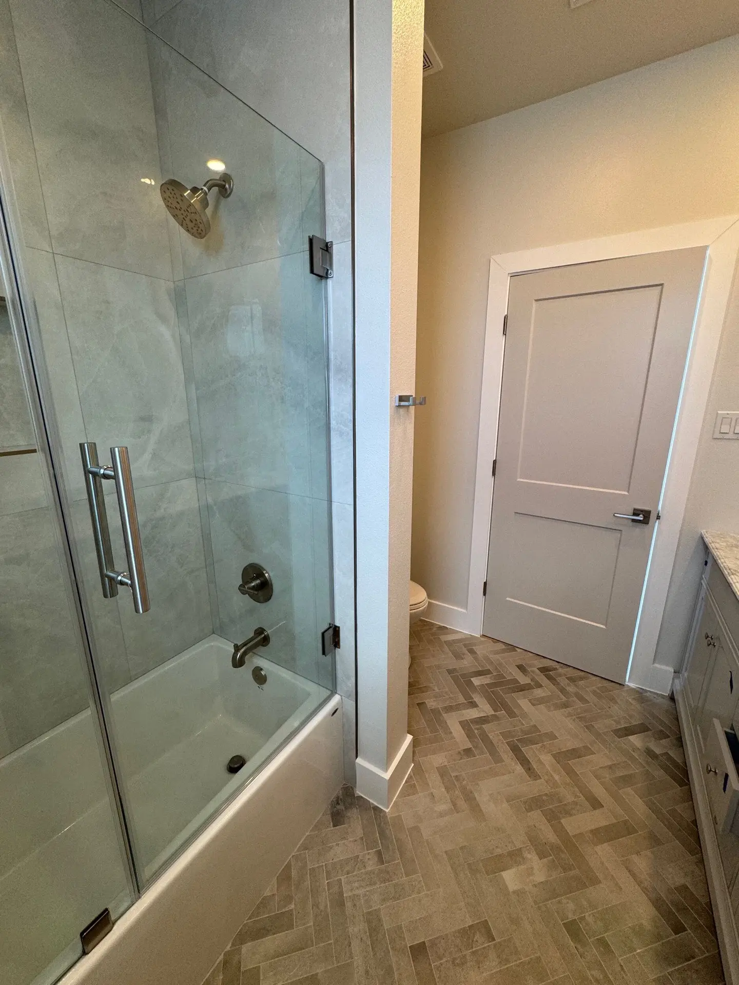 Primary shower interior with white marble wall tile, hexagonal floor tile pattern, brass rain showerhead, and frameless glass door