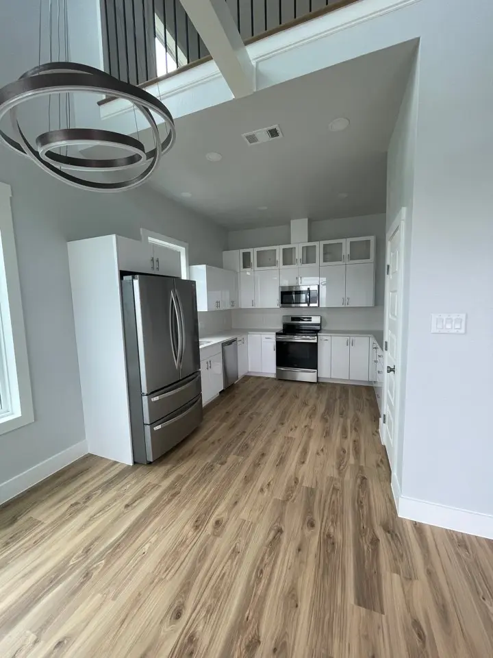 Spacious open-concept living room with vaulted ceiling, oversized windows on multiple walls, and light wood-look plank flooring throughout