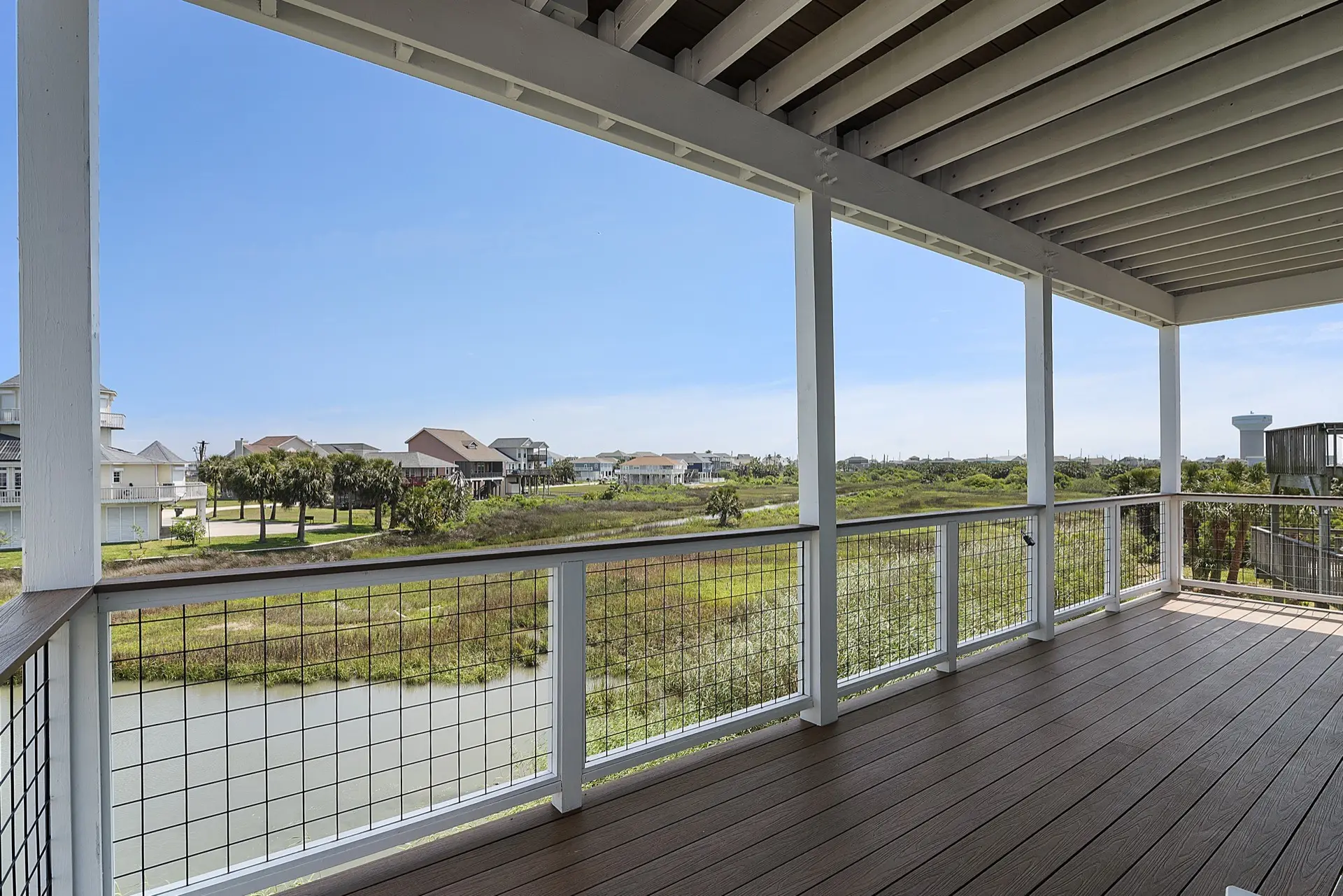 Upper-level balcony with cable railing overlooking the canal, marsh grasses, and distant Galveston Bay from 3742 Laguna
