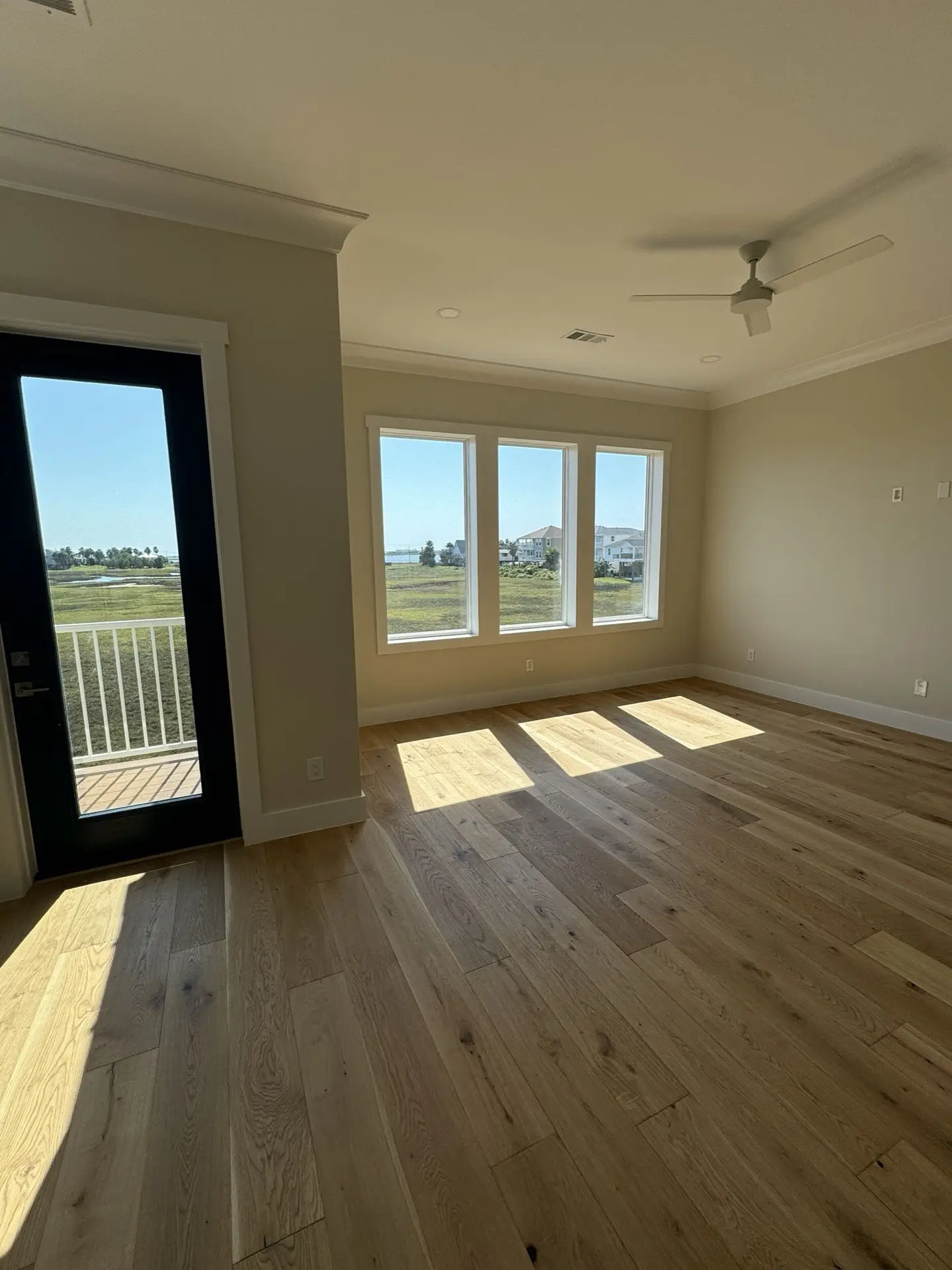 Master bedroom with oak hardwood floors, crown molding, large windows facing West Bay, and warm neutral wall tones